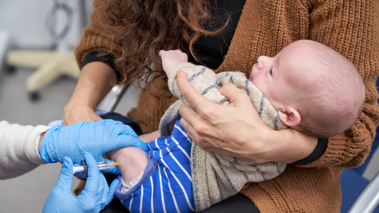 Doctor is giving a baby an injection while his mother is holding him in her arms