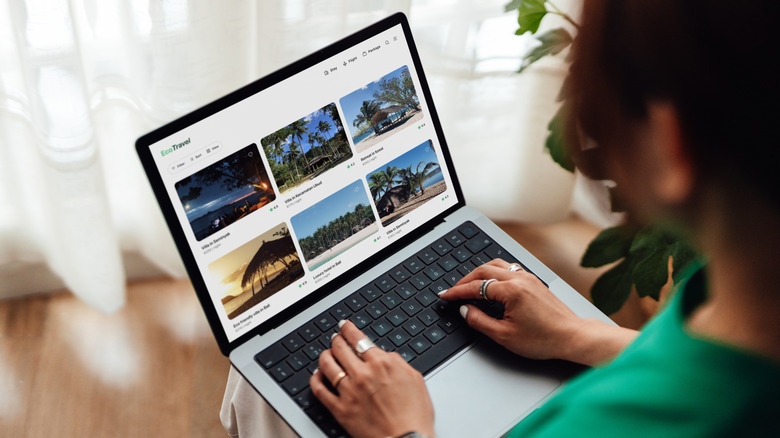 Young woman using laptop showing online travel booking platform with various sustainable hotels