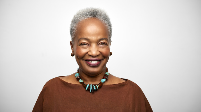 Woman with grey hair smiling, wearing costume jewelry