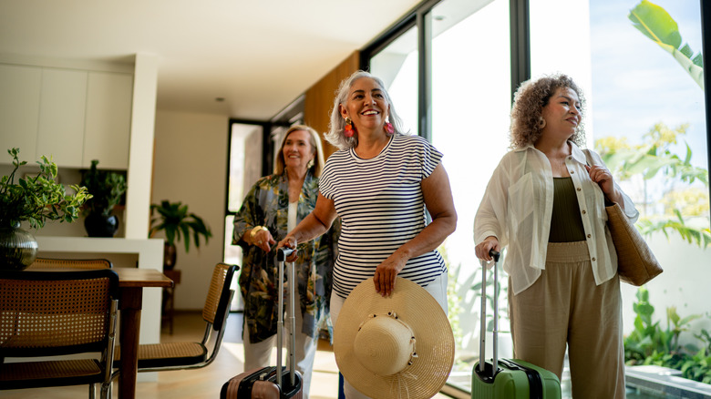 Three senior women in a luxury hotel room with luggages and sunhat