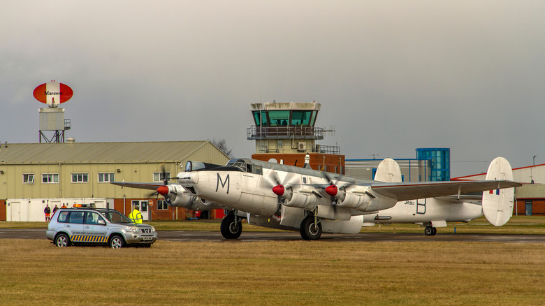 An old military plane taxiing at Coventry Airport during a Royal Air Force show with a small airport control tower in the background.