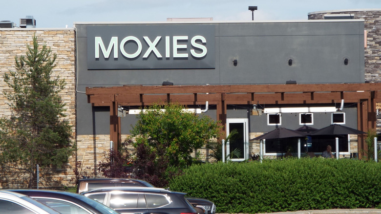 An exterior of Moxies shows outdoor seating, the iconic sign, and a pergola over the patio