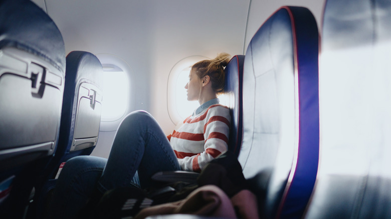a young woman looking out of a plane window with two empty seats next to her