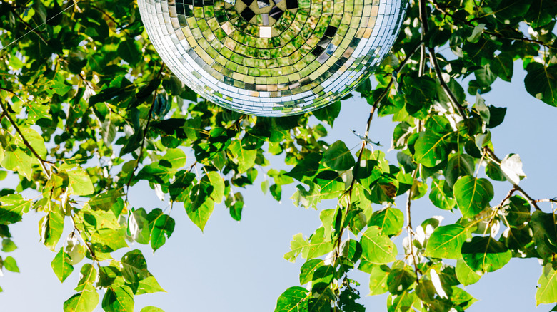 Large disco ball hanging outside surrounded by greenery