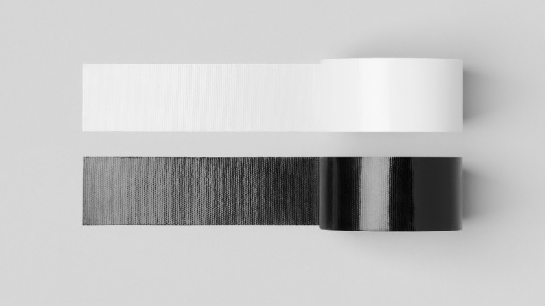 Two roles of tape, one black and one white, unrolled on a grey surface