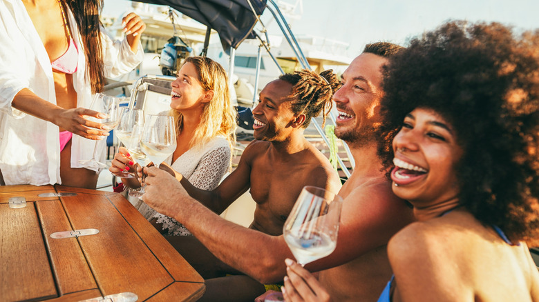 A diverse group of Millennial-aged people toast wine glasses on a boat