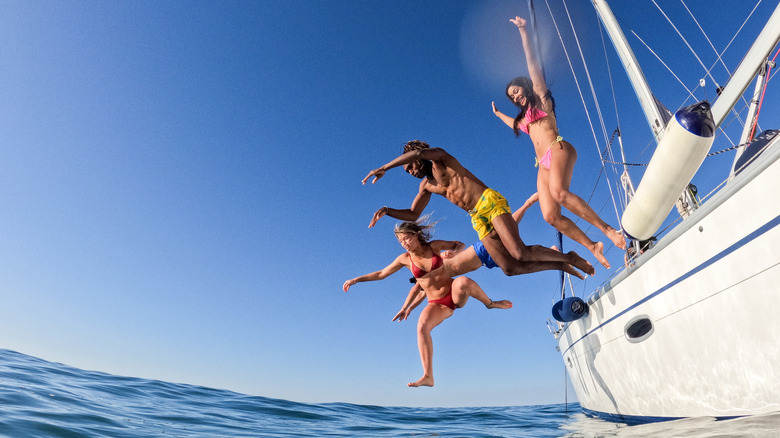 A trio of young people jump off a yacht into the sea