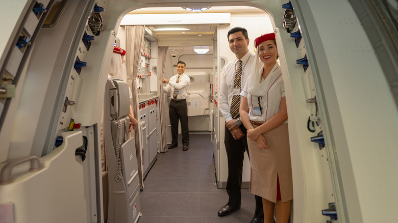 Three flight attendants stand inside boarding door and smile out at camera