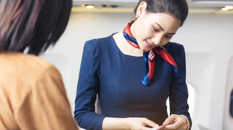 Flight attendant in blue outfit looks down at passenger ticket