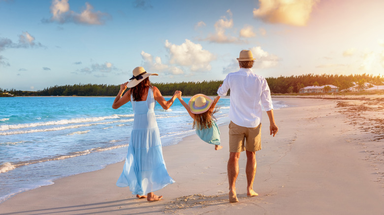 a couple swings their daughter between them as they enjoy a walk on the beach at sunset