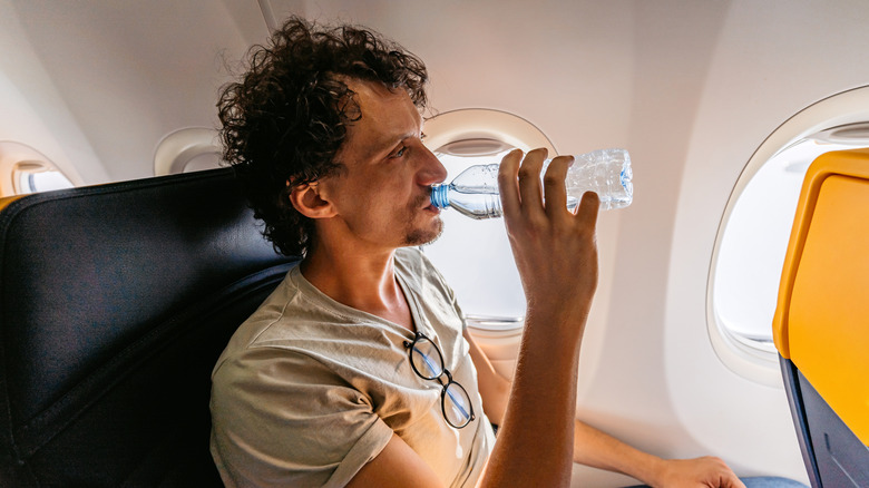 A man drinks water on a airplane.