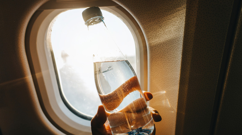 A capped water bottle is held up in front of an airplane window.