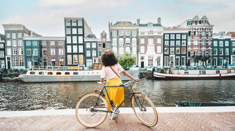 A woman with a bicycle looks out at the canal in front of her in Amsterdam, Netherlands