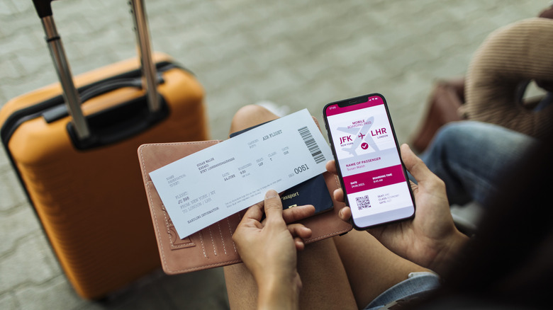 A person holds up a boarding pass, ticket, and passport at an airport
