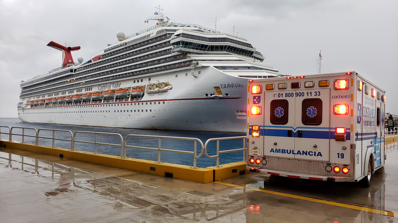 An ambulance parked on a pier next to a large Carnival cruise ship