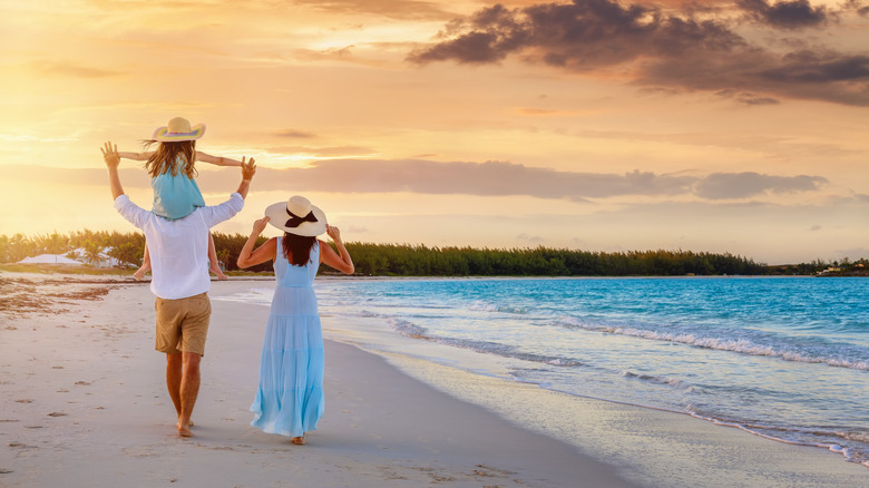 A family relaxedly walks down the beach in the tropics