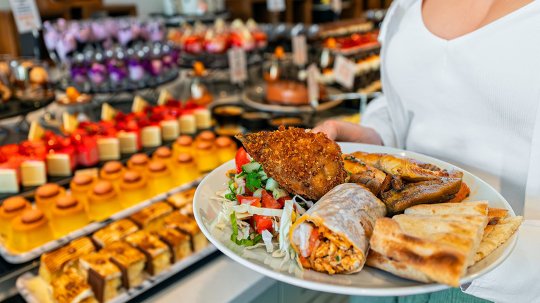 A woman holding a plate stacked full of food at a buffet.