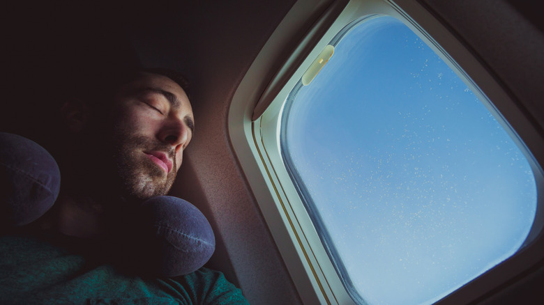 Man sleeping on plane next to the window