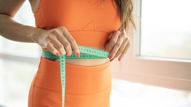A woman in orange exercise clothes measures her waist