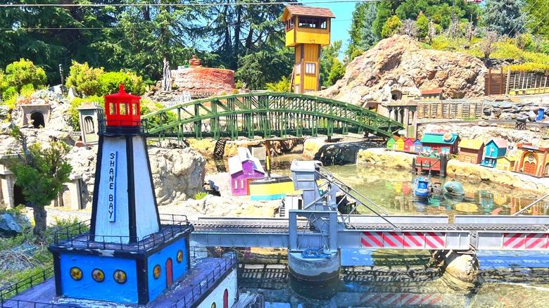 A miniature train track runs through a miniature city with a lighthouse, bridges, and houses at the Medford Railroad Park