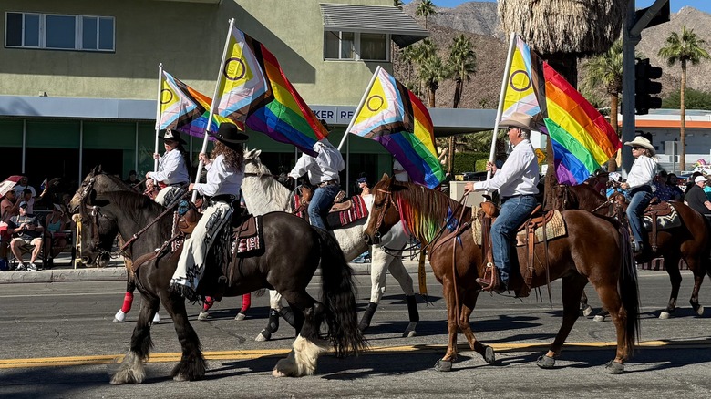 Riders on horseback holding rainbow LGBTQ flags during the pride parade at the Palm Springs Hot Rodeo.