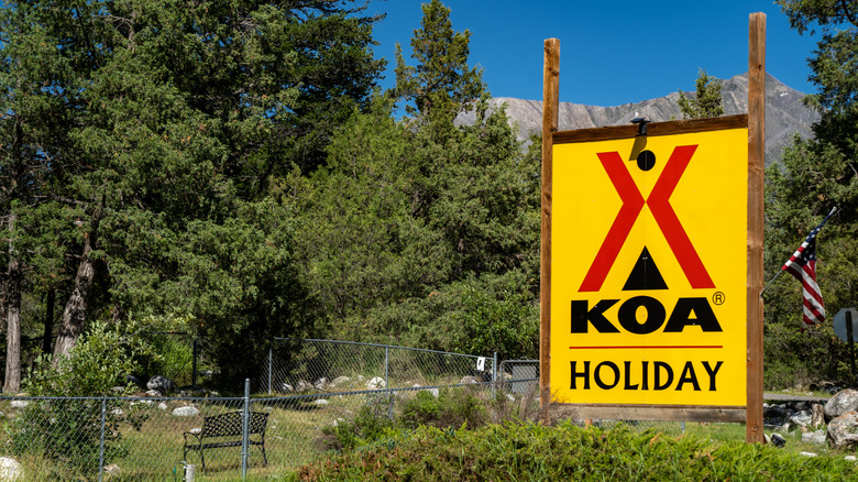 A large, yellow KOA sign displayed on a hill covered in trees.
