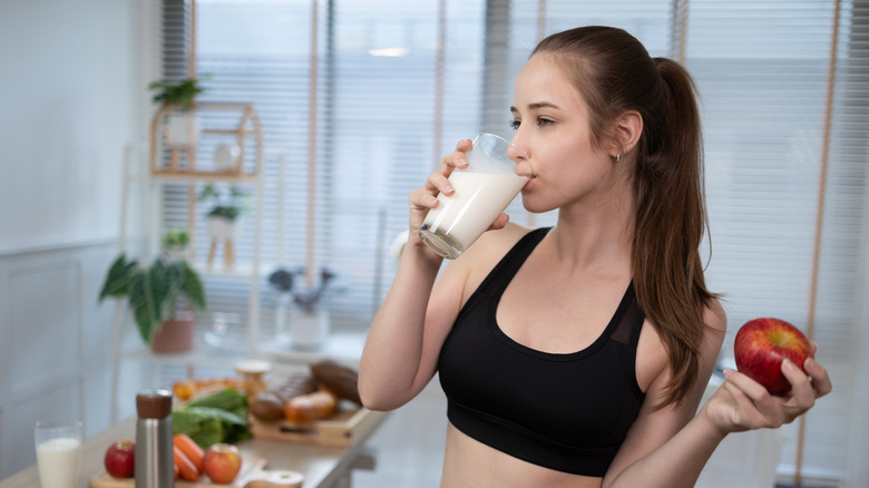 An athletic woman drinks a glass of milk in a kitchen