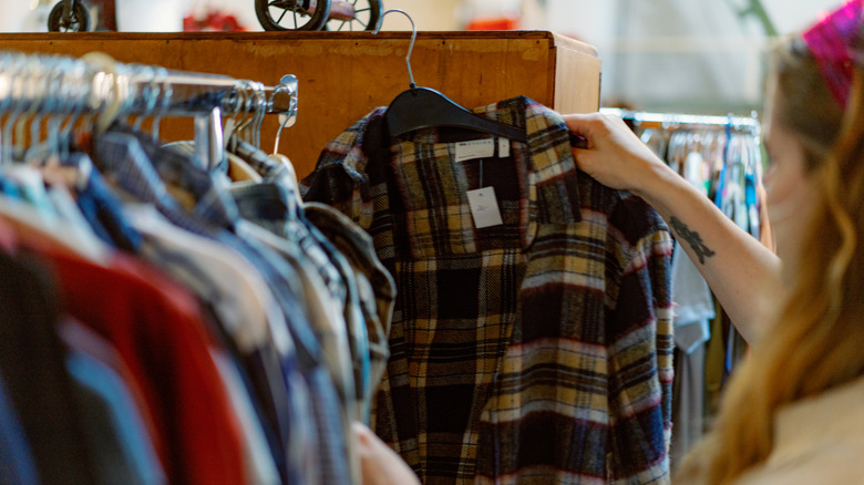 Young woman holds up a flannel shirt while shopping at thrift store