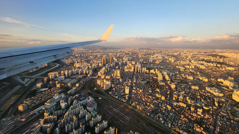 A view of Seoul from an airplane window during golden hour, with an airplane wing in the foreground
