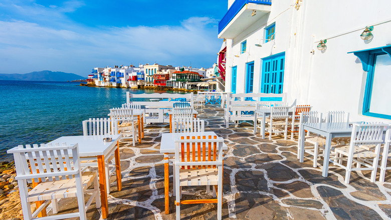 Wooden tables on a stone patio overlook the sea in Mykonos, Greece.