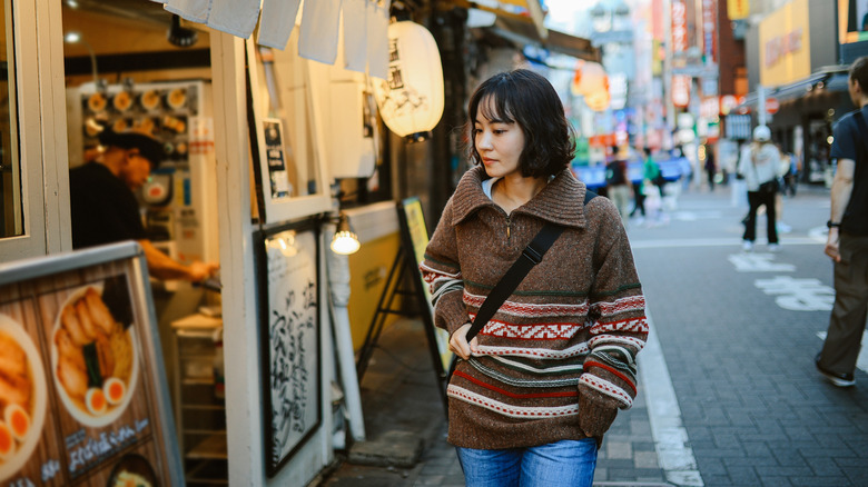 A woman glancing down at a ramen menu outside a shop entrance