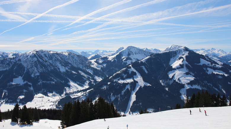 A wide shot of mountain peaks in the Alps with skiers in the foreground