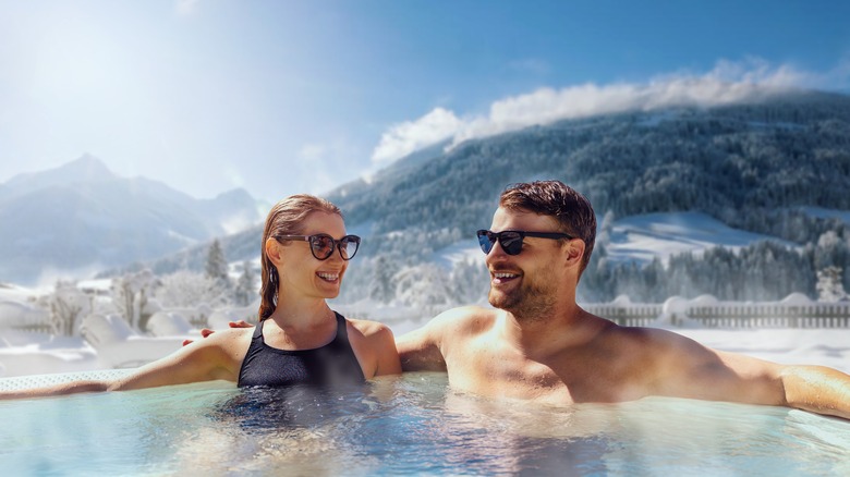 A couple relaxing in a hot tub with snowy mountains behind them