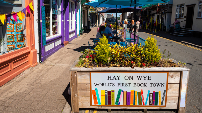 Sign that says Hay on Wye World's First Book Town with colorful storefronts in the background