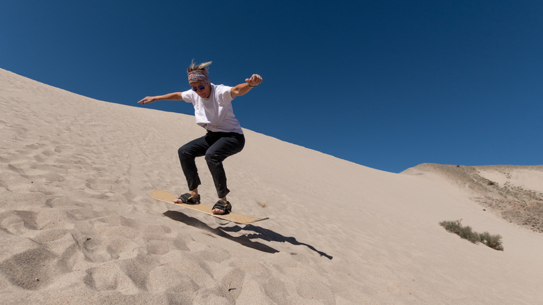 Woman sandboarding down steep sand dune