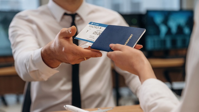 An airline worker is handing a passport with airline ticket to a passenger at an airport check-in counter