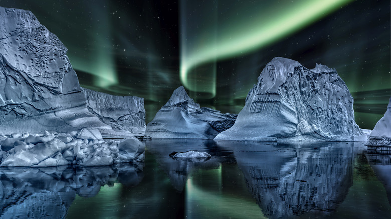 Icebergs and their reflections in the sea in Greenland, pictured at night and lit up by the green lights of the aurora borealis above