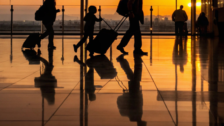 People drag their suitcases through airport at sunset