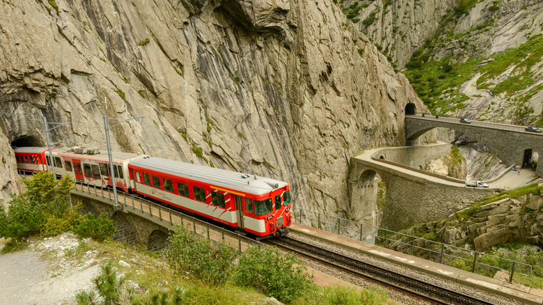 Red train near the historic stone Devil's Bridge at Gotthard Pass in Switzerland