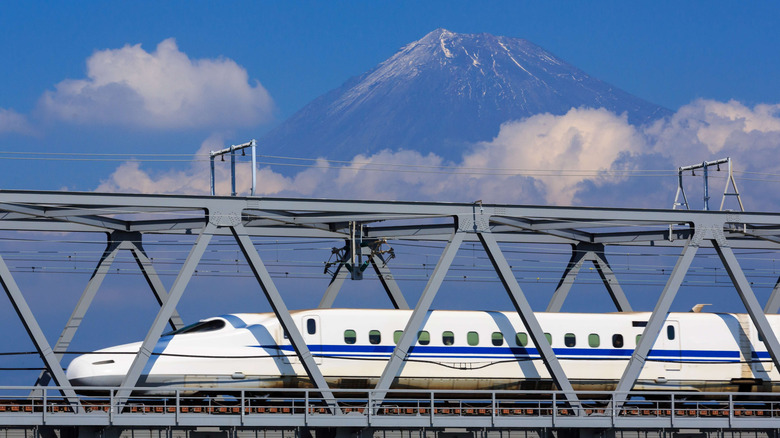 Daytime image of Japan's Shinkansen (bullet train) cruising by, with Mount Fuji clearly visible above the clouds in the background