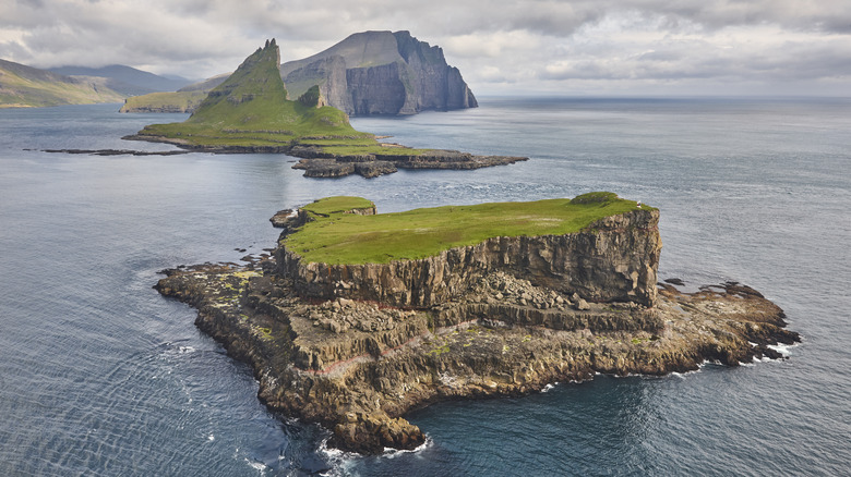 Rugged cliff walls topped by green meadows on a remote island viewed from a helicoper