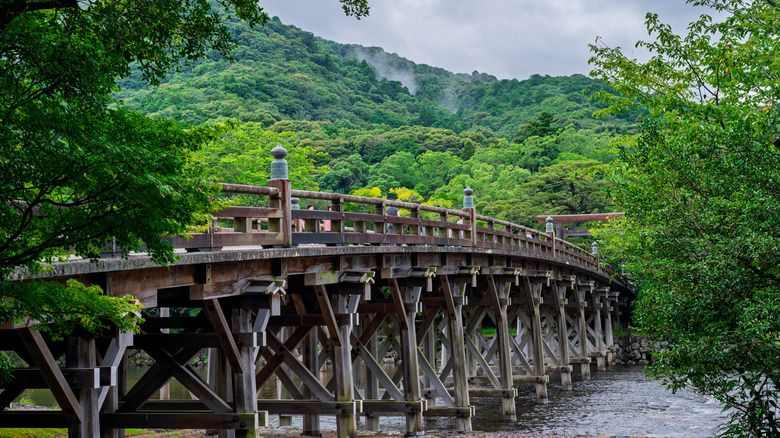 An ancient bridge cuts through a river in Japan amidst a lush green landscape