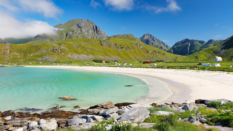 The crescent-shaped Haukland Beach in Norway with white sand, clear turquoise water, and surrounding mountains.