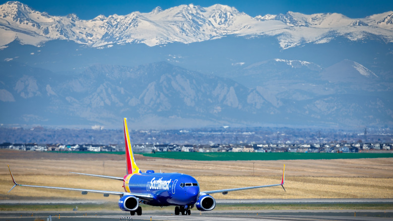 A blue jet with "Southwest" written on the side on the runway in Denver airport with the snow-capped mountains in the background
