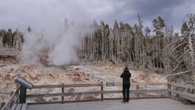 A tourist taking a photo of Steamboat Geyser in Yellowstone National Park