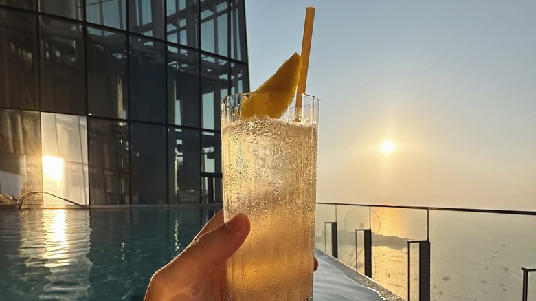 A hand holding a drink in front of the pool at Ciel Dubai Marina, Vignette Collection