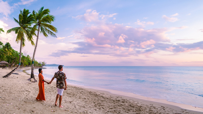 a couple holds hands on a sandy, clean beach in St. Lucia as they watch the sunset