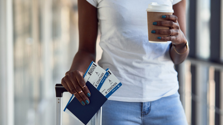 Person holding a coffee cup and passport at an airport