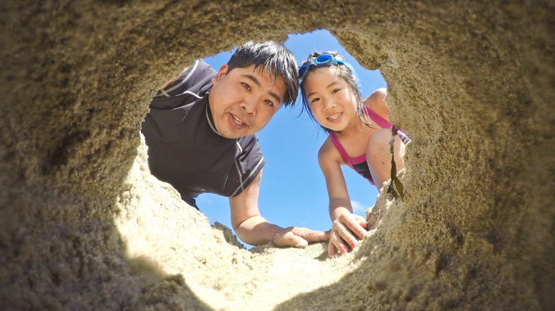 A girl and her father peering inside a hole they dug in the sand