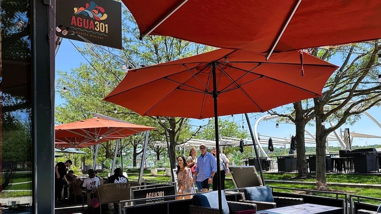 Outdoor patio of Agua 301, a Mexican restaurant at Yards Park in D.C., featuring orange umbrellas, patrons dining, and walking.